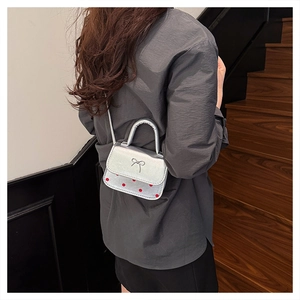Mini sac argenté à pois rouges et nœud élégant porté par un mannequin vintage