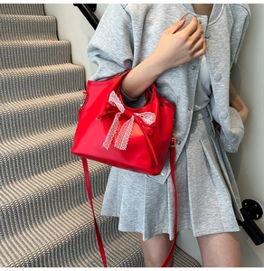 Detalle de bolso tote de cuero rojo con un lazo de encaje blanco y herrajes plateados