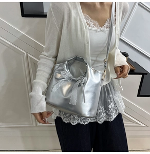 Detalle de bolso plateado metalizado con lazo de encaje blanco y correa fina ajustable