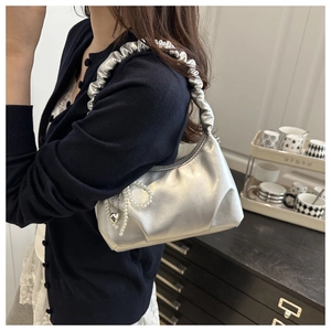 Detail of silver metallic shoulder bag featuring a pleated handle and pearl heart charm