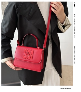Red pebbled leather crossbody bag with SM logo shown on a model in a black blazer