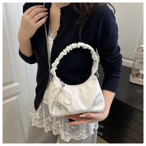 Close-up of white crescent bag with ruched handle, pearl bow charm, and chain strap