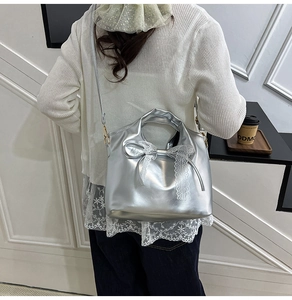 Detalle de bolso de cuero plateado con lazo de encaje blanco y elegante correa al hombro