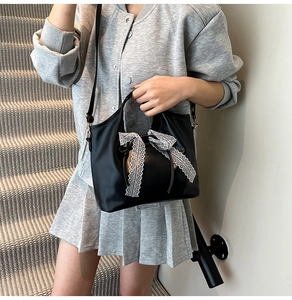Detalle de un bolso negro con un lazo grande de encaje blanco y correa de hombro ajustable