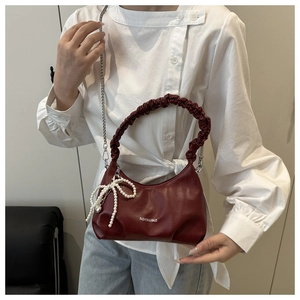 Detail of burgundy textured shoulder bag with pleated handle and pearl bow charm