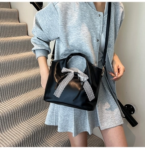 Detalle de bolso de cuero negro con lazo de encaje blanco y hebilla dorada