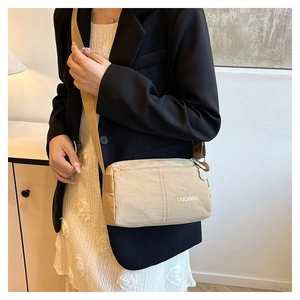 Detail of beige nylon crossbody bag with wide strap and printed logo on black blazer