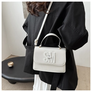 Close-up of white pebble leather handbag featuring a prominent SM metal logo on the flap