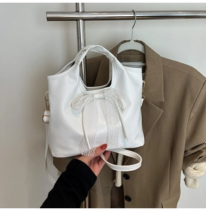 Detalle de un bolso blanco de cuero con un elegante lazo de encaje y ganchos dorados