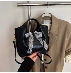 Detalle de bolso en cuero PU negro con un gran lazo de encaje blanco y correa ajustable