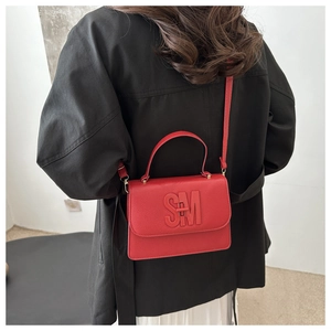 Detail of red pebbled leather tote with SM embossed logo shown on a black coat