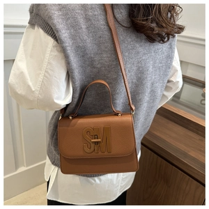 Close-up of brown litchi pattern leather square bag with elegant SM metal buckle detail