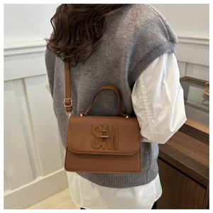Brown litchi grain crossbody bag with SM logo worn on back with adjustable shoulder strap