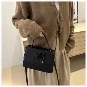 Close-up of black pebble leather handbag featuring prominent SM metal logo on the front flap