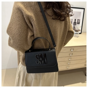 Close-up of black lychee grain leather handbag with SM logo worn by a model