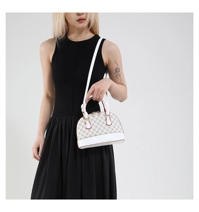 Detailed view of monogrammed shell bag with red piping and white leather shoulder strap