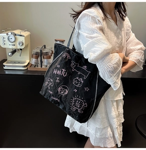 Detail of black tote bag with pink cat graffiti and crinkled texture in a cafe setting
