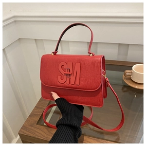 Detail of red litchi texture handbag with SM metal buckle on a cozy indoor coffee table