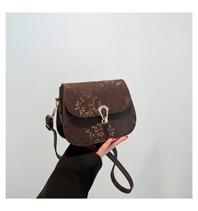 Détail d'un sac bandoulière marron foncé motif serpent avec fermoir en métal doré en U