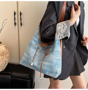 Dettaglio della borsa tote in denim blu con fiocco in pelle e perline sulla tracolla
