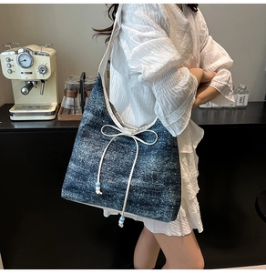 Dettaglio di una borsa tote in denim blu con fiocchi bianchi e spalline a contrasto