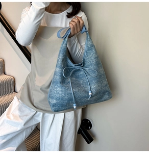 Dettaglio della borsa hobo in denim blu con fiocco decorativo e perline bicolore