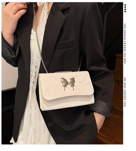 Detail of a creamy white butterfly buckle shoulder bag with elegant metal chain strap