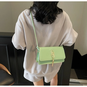 Detail of mint green crossbody bag with gold SS logo and tassel on grey outfit