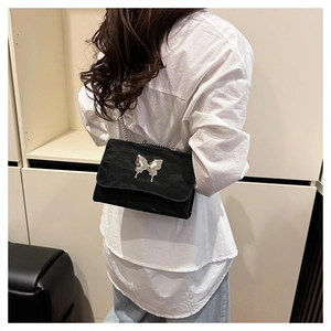 Detail of black underarm bag with silver butterfly emblem and metal chain strap on model
