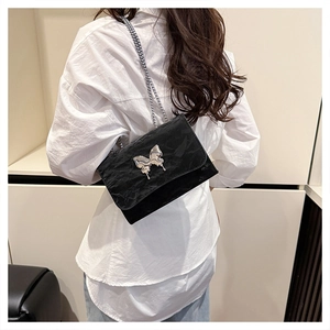 Detail of black glossy butterfly shoulder bag with silver chain on white shirt