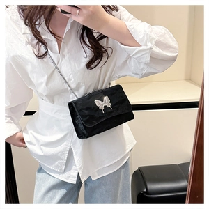 Detail of black velvet shoulder bag with silver butterfly buckle and chain strap on person