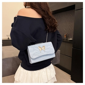 Close-up of light blue pleated handbag featuring a golden butterfly metal clasp and chain