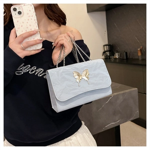 Close-up of light blue pleated bag with gold butterfly metal clasp and delicate chain