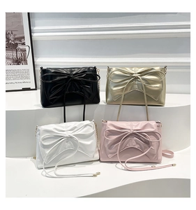 Collection of bow-knot chain bags in black, gold, white, and pink displayed on steps