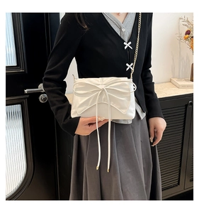 Close-up of a white leather crossbody bag featuring a large bow and gold chain strap