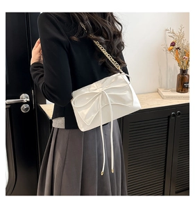 Detail of white faux leather crossbody bag featuring a large bow and gold chain strap