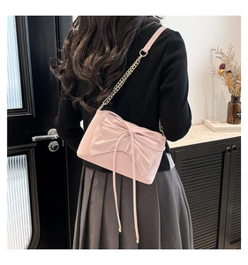 Rear view of model wearing pink bow crossbody bag with gold chain strap on grey pleated skirt