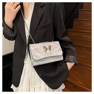 Detail of light blue pleated chain bag with gold butterfly accent worn on a black suit