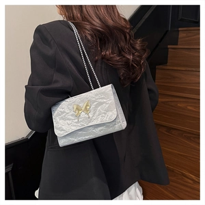 Detail of silver pleated shoulder bag with golden butterfly clasp and metal chain strap