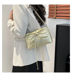Detail of light gold crossbody bag featuring large 3D bow and woven chain strap