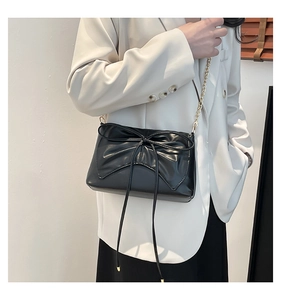 Chic black crossbody bag with bow detail and gold chain strap styled on a model