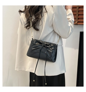 Detailed shot of a black PU leather bag with a giant bow and golden chain strap