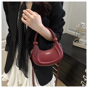 Detail view of burgundy crescent moon handbag with thick handle and fashion text logo