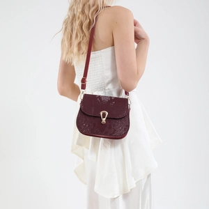 Sac à bandoulière rouge vin motif serpent avec boucle dorée sur une robe blanche
