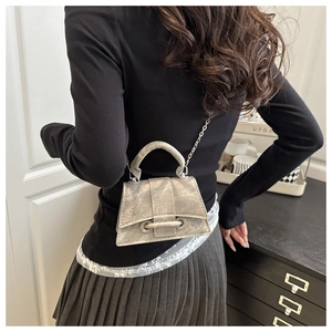 Close-up of a silver metallic trapezoid crossbody bag with chain strap on a model