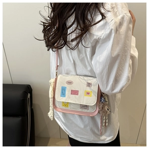Detail view of cream white square crossbody bag with pink trim and bear charm on model
