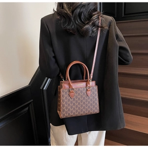 Détail d'un sac cabas en cuir marron avec motif en M porté à l'épaule d'un mannequin