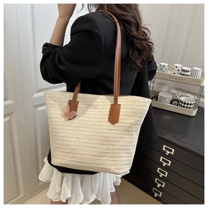 Detail of a large beige woven straw tote bag with brown leather handles and pink charm