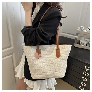 Detail of a woven straw tote bag with brown leather handles and pink lace butterfly charm