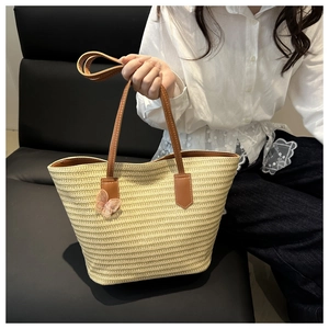 Détail du sac cabas en paille tissée avec anses en cuir marron et breloque papillon rose